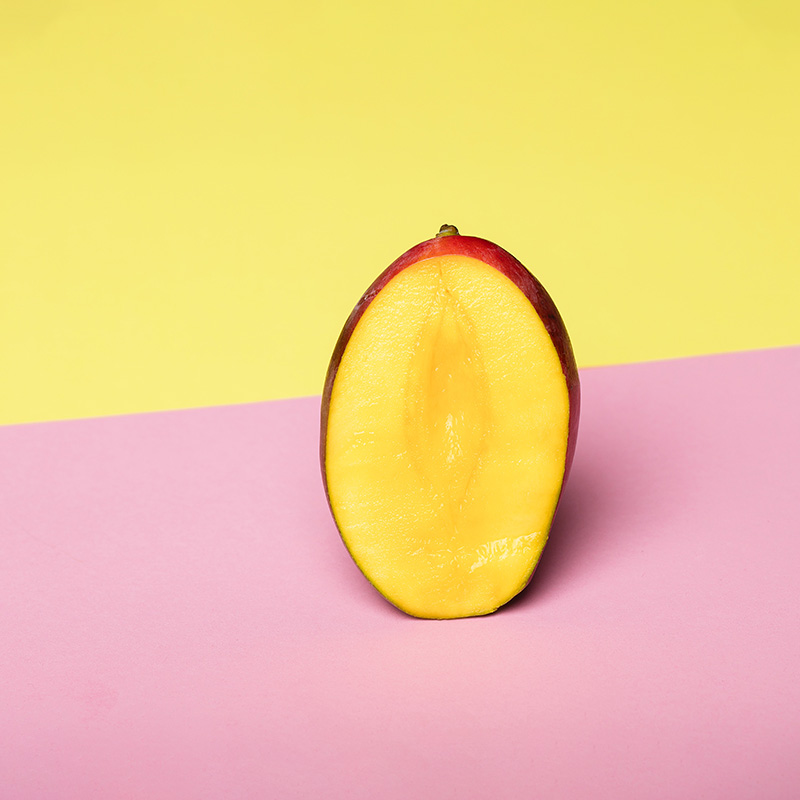 Mitad de un mango vibrante y jugoso sobre un fondo bicolor amarillo y rosa.